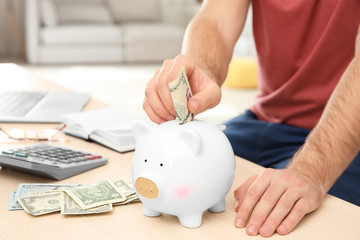 Obraz na płótnie Canvas Man putting money into piggy bank, closeup