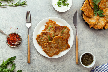 Potato latkes traditional jewish pancakes with sour cream, parsley, dry red pepper flakes and mint sauce. Background, white napkin with blue flowers. Hannukah celebration dish concept.