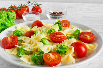 Broccoli farfalle pasta with tomato cherry in white plate on wooden table