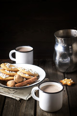 Christmas coookies in vintage plate and two mugs with hot beverage on old wooden table.