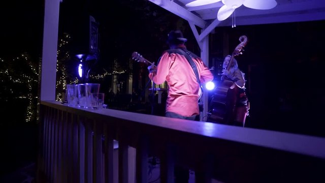 Pushing into band in blue lights as guitarist rocks to the music at an outdoor cafe.