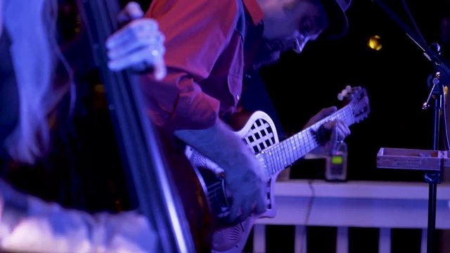 Closeup of a roots musician rocking out on a resonator guitar at night at a restaurant.