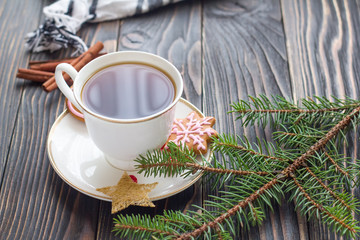 Cup of tea, fir branch, red berries, ginger cookies and cinnamon on wooden table