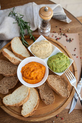 three different kind of hummus : hummus of spinach, hummus paprika and classic hummus with bread sliced on a wooden board