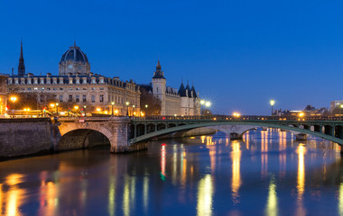 Conciergerie Building in Paris, France at night with lights reflection in the Seine River water.