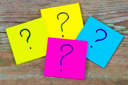 questions, decision making or uncertainty concept - a pile of colorful sticky notes with question marks on wooden background
