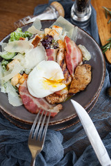 Caesar salad with bacon and poached egg on a wooden table