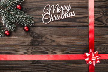 View from above of a Merry Christmas inscription on dark brown wooden background with red ribbon...
