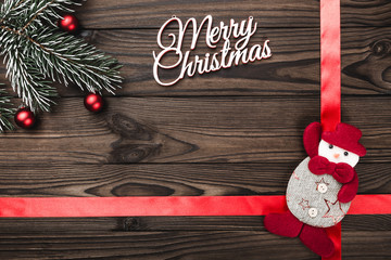 View from above of a Merry Christmas inscription on dark brown wooden background with red ribbon...
