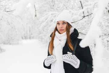 Beautiful young girl in a white winter forest wearing a white hat with white sleeves