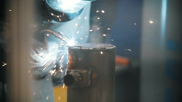 The welder welds metal parts at the plant, industrial welding