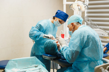 Male old professional dentist surgeon in uniform and female assistant helps to performing operation...