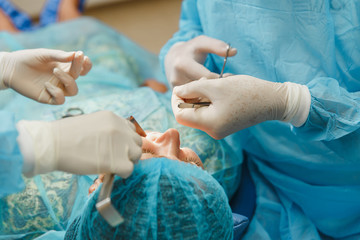 Male old professional dentist surgeon in uniform and female assistant helps to performing operation...