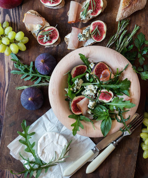 Easy diet salad with arugula, figs and blue cheese on a brown wooden surface. Sandwiches with ricotta, fresh figs, prosciutto, rosemary and blue cheese. Delicious fruity breakfast, top view