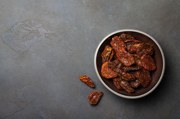 Sun-dried tomatoes in a dark bowl on a dark stone slate background. Copy space, horizontal image, top view