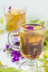 Linden herbal tea in a transparent grog glass with a linden blossom and bunch of herbs on the white...