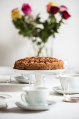 Fresh homemade apple cake on a laid table with white table cloth and a vase of roses, shot from the side