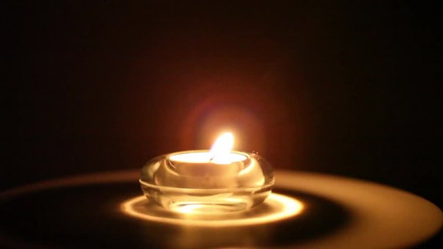 The flame of a small candle illuminates the night before it is extinguished by the blowing of the wind
