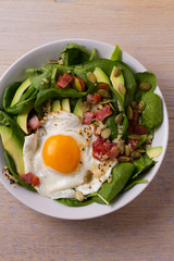 Egg with quinoa, avocado, bacon, spinach and pumpkin seeds in white bowl. Ideal dish for breakfast. View from above, top, horizontal