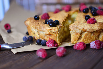 Appetizing pie with berries on a wooden table. A piece of very tasty home-made pie. Charlotte with apples, decorated with berries.
