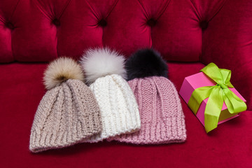 Fototapeta na wymiar winter knitted hats with a fur ball lay on the red couch. knitted hats and a New Year's gift