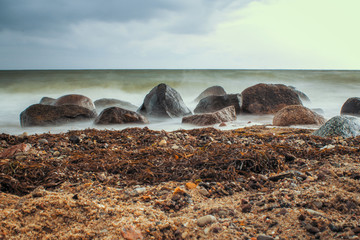 Steine am Strand mit Wellen, Seetang und Gischt