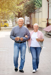 Mature couple with cups of coffee walking together outdoors