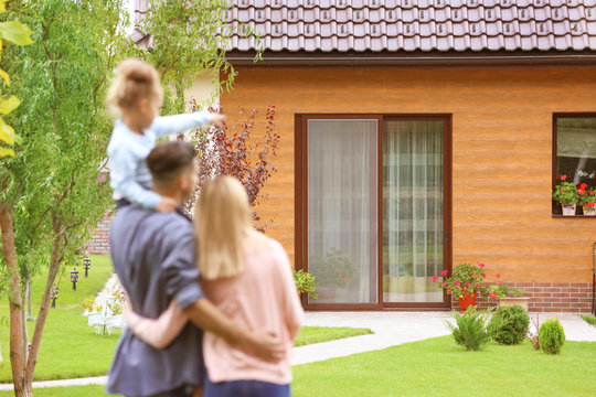 Happy Family Standing In Courtyard And Looking At Their House