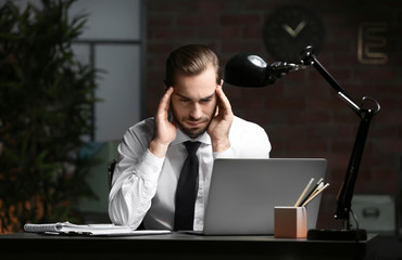 Tired young man using laptop in office at night