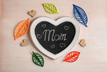 Heart-shaped chalkboard with word "Mom" on light background