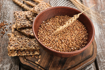 Bowl with raw buckwheat and seed crispbread on wooden board