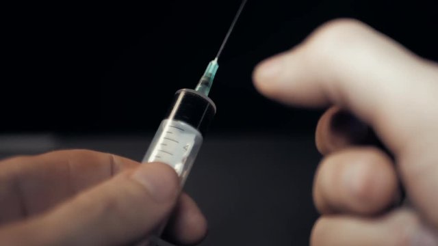 Slow motion of hand getting a hypodermic syringe. Addict preparing for getting drug dose injection. Man's finger knocks on the syringe