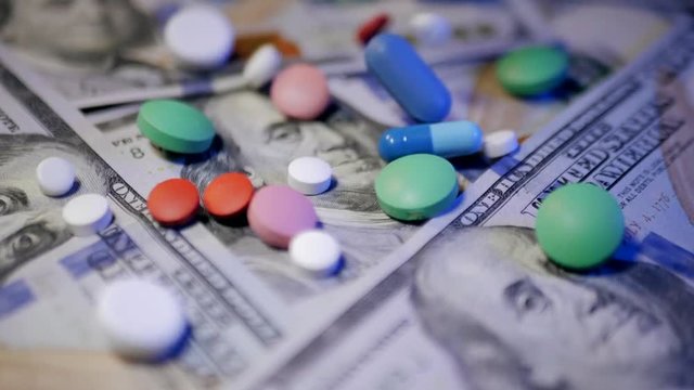 Pills falling on dollar banknotes, expensive medication, pharmaceutical business. Pharmacy theme. Multicolored Pills and Capsules on money. Slow motion.