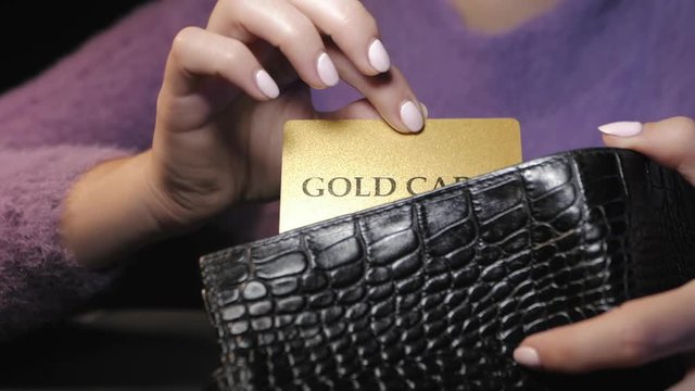 Woman's hand gets a gold credit plastic card from wallet. Slow motion