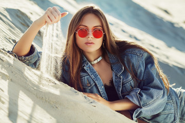 Portrait of young beautiful woman wearing stylish light blue denim jacket, red round sunglasses....