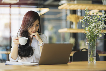 Beautiful asian woman using laptop at cafe while drinking coffee, Relaxing holiday concept.
