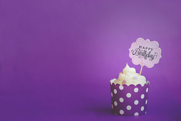 Vanilla cupcake with small decorative hearts and happy birthday sign, in violet baking paper cup,...