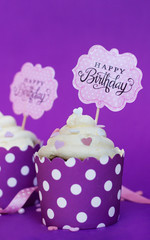 Cupcake with small decorative hearts and happy birthday sign, against violet background