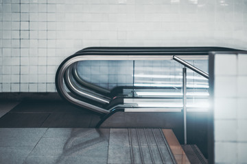Side view of modern glass and chrome escalator in urban underground with white tiles in background;...