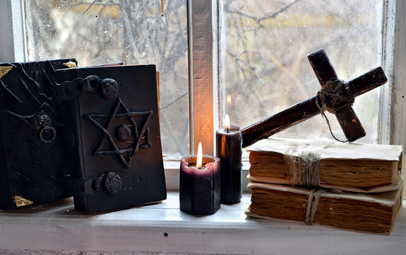 Black magic books, black candles and cross against old window. Occult, esoteric, divination and wicca concept, mystic background
