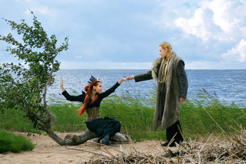 guy holds the hand of a woman sitting on a tree on the shore of the sea