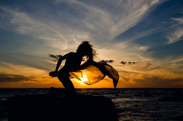 Silhouette of woman sitting on rock at sunset