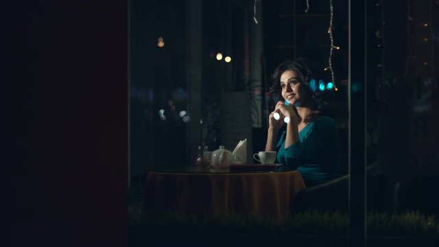 Woman with a smartphone in a cafe.
Slow motion. A pretty woman is sitting in a cafe behind the glass and communicates on the phone.
The glass reflects the traffic of urban transport.