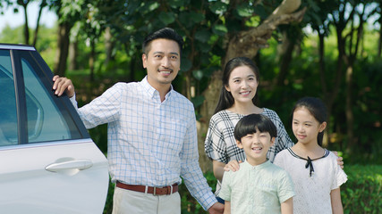 Asian family standing beside car looking forward and smiling