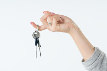 Hand of business woman or real estate agent with keys from new flat or house hanging on the finger. She welcomes to buy a flat or house. Isolated on white background