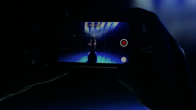 People records a video from a concert of a beautiful singer on a smartphone.