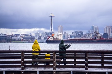 Two people fishing off a dock with the Seattle skyline in the background - 184376016