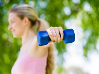 Portrait of cheerful woman in fitness wear exercising with dumbbell