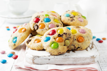 Stack of children's cookies with colorful chocolate candies in a sugar glaze on a white light wooden background. Selective focus
