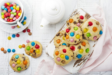 Children's cookies with colorful chocolate sweets in sugar glaze on white wooden background. Selective focus. Top view. Place for text.
